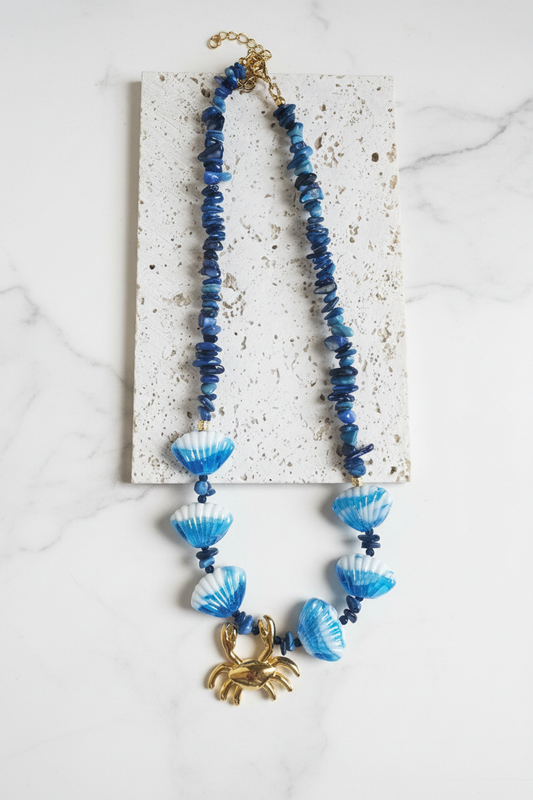 Blue beaded necklace with a gold crab pendant on a white background