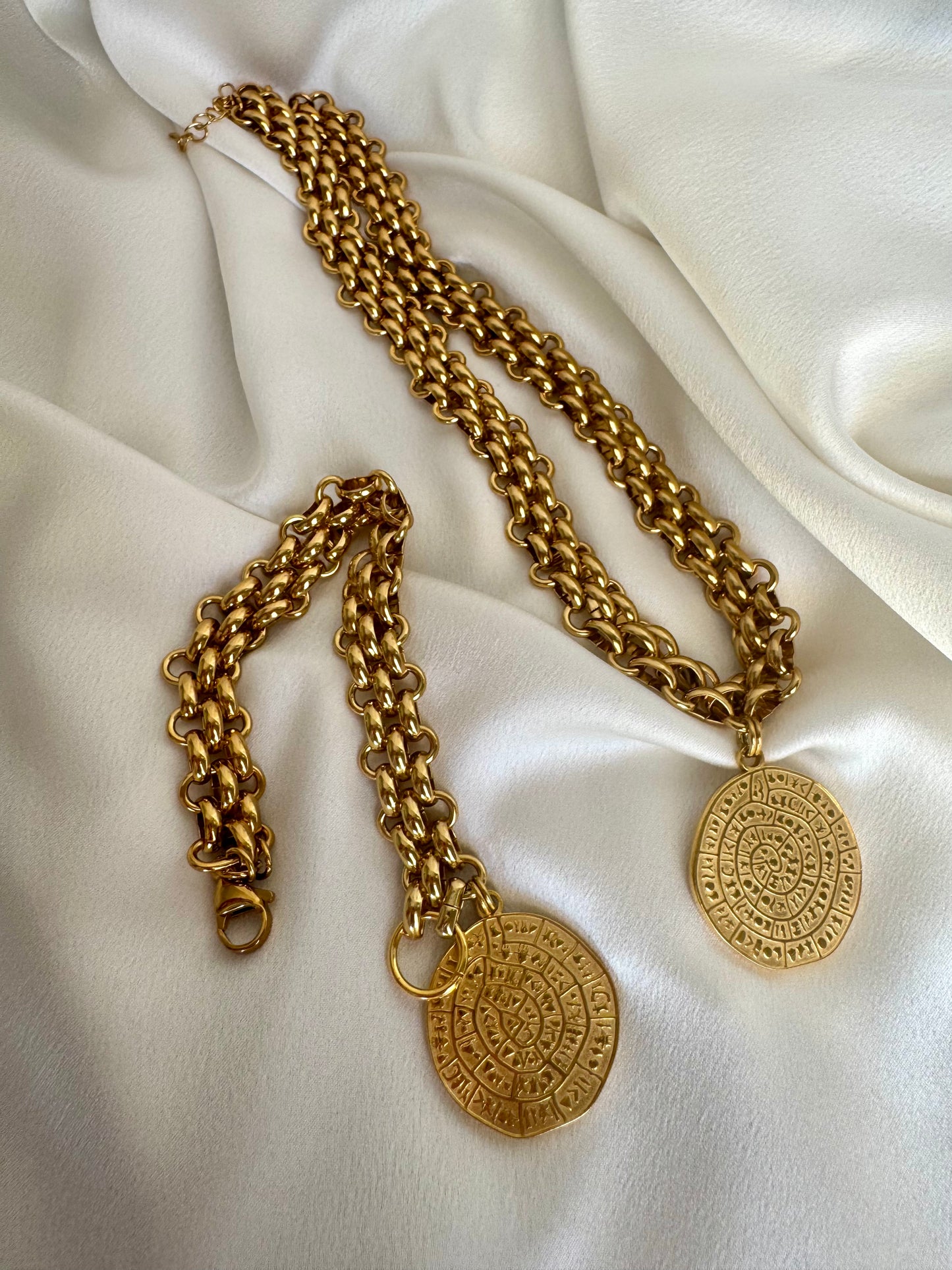 Gold chain necklace with circular pendants on a white fabric background
