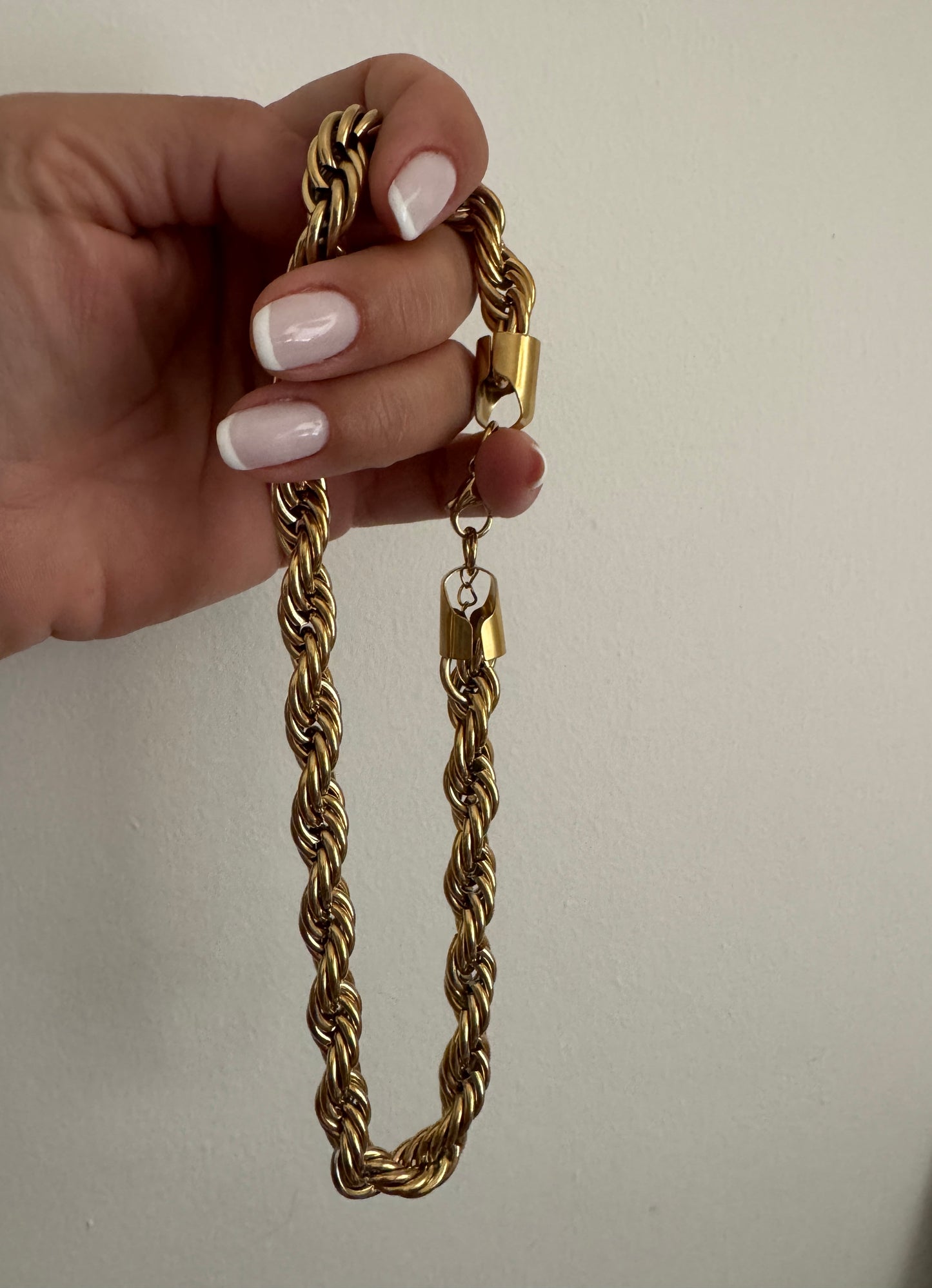 Gold chain with a lock held by a hand against a plain background