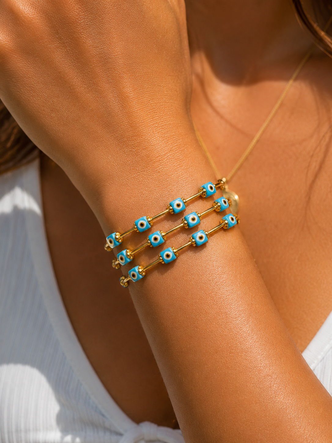 woman's wrist wearing a bracelet with gold elements and turquoise evil eye beads
