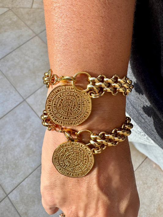 Gold bracelet with circular medallions on a wrist against a neutral background