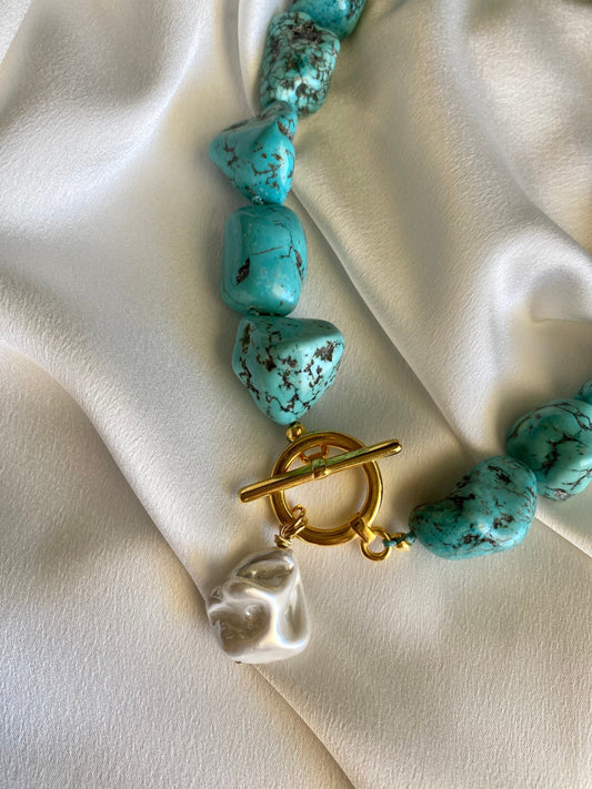 Turquoise beaded necklace with a gold clasp and mother of pearl pendant closeup