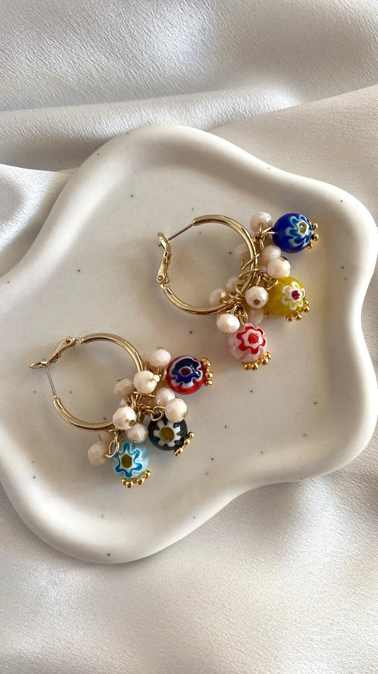 A pair of brass hoop earrings with millefiori glass beads and freshwater pearls, displayed on a white plate.