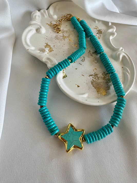 Turquoise beaded necklace with a gold star pendant on a white surface