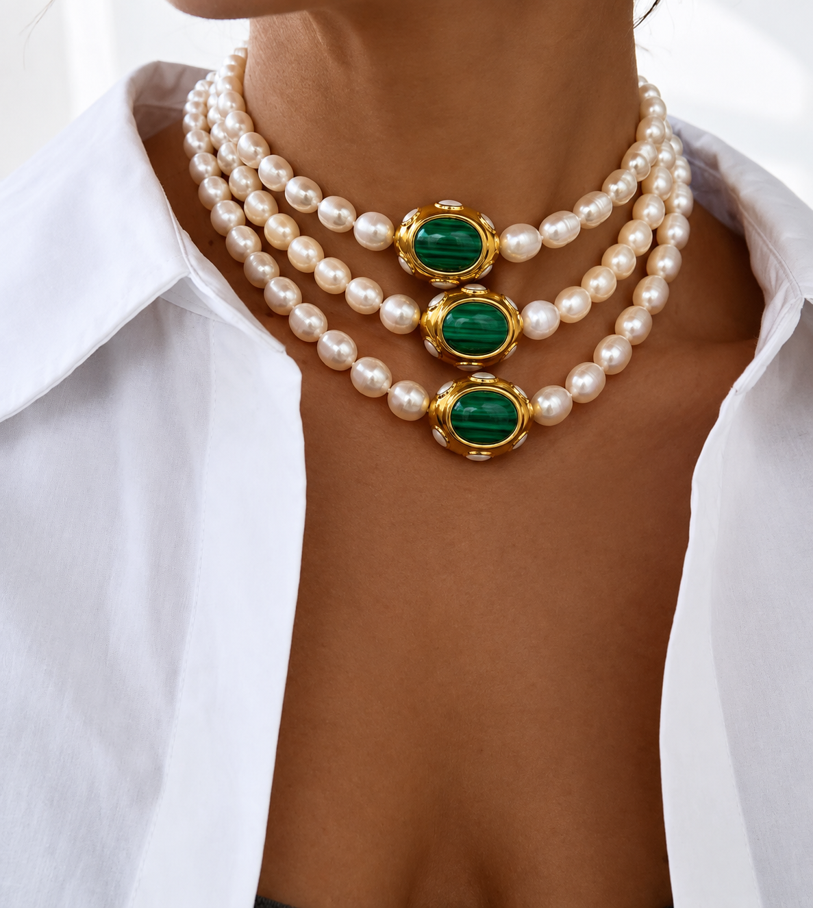 A close-up of a model wearing on neckline AIGLI pearl and green malachite necklace worn , styled with a white collared shirt.