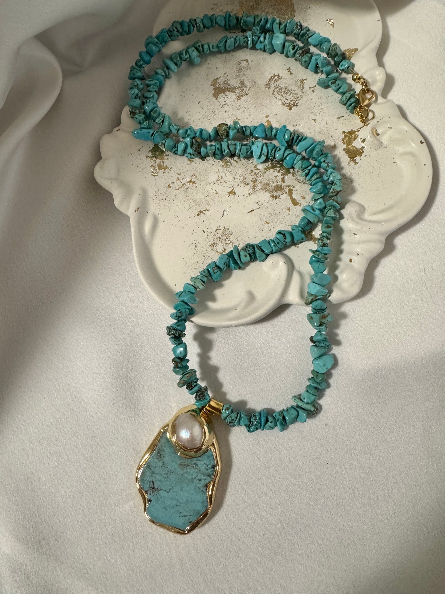 Turquoise beaded necklace with a pendant on a white surface 