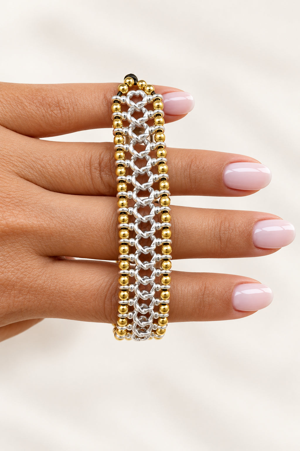 Hand wearing a gold and silver bracelet against a beige background
