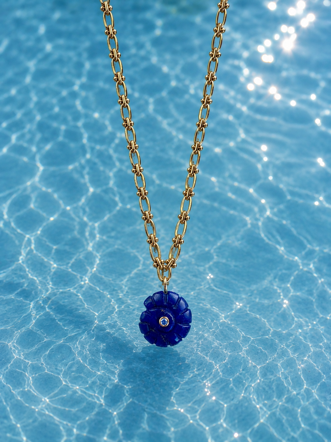 Gold necklace with a blue shell pendant on a blue water background