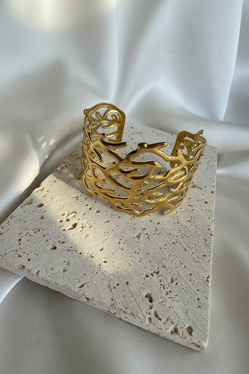 Gold coral-shaped bracelet on a textured stone surface with white fabric background