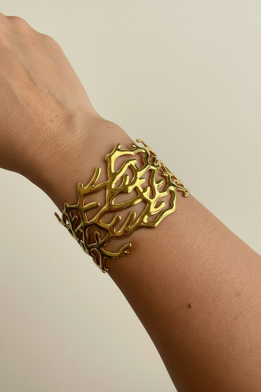 Gold coral bracelet on a wrist with a white fabric background
