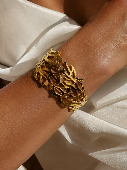 Gold coral bracelet on a wrist with a neutral background
