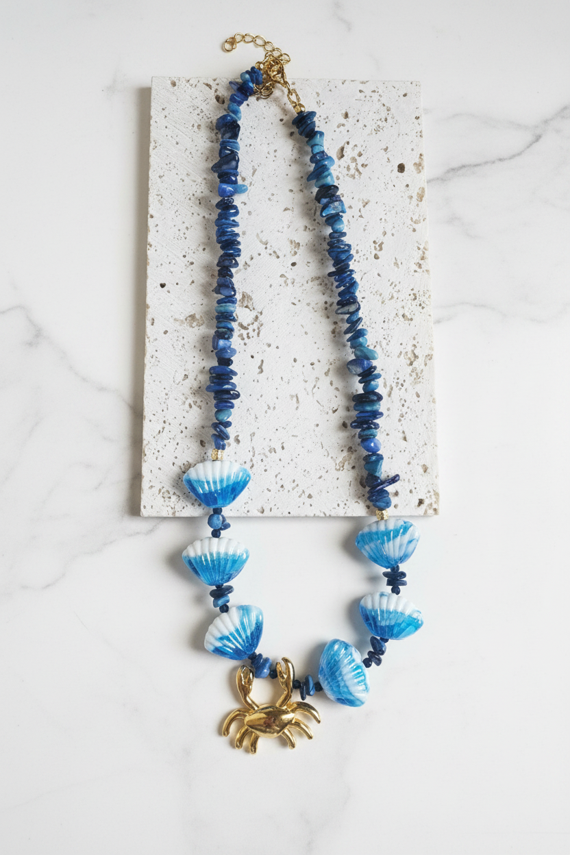 Blue beaded necklace with a gold crab pendant on a white background