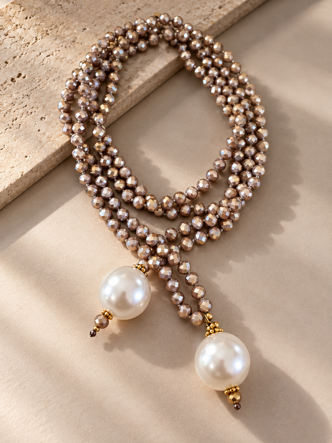 A multi-strand beaded necklace with white faux pearls and gold-toned accents, draped elegantly on a beige textured surface.