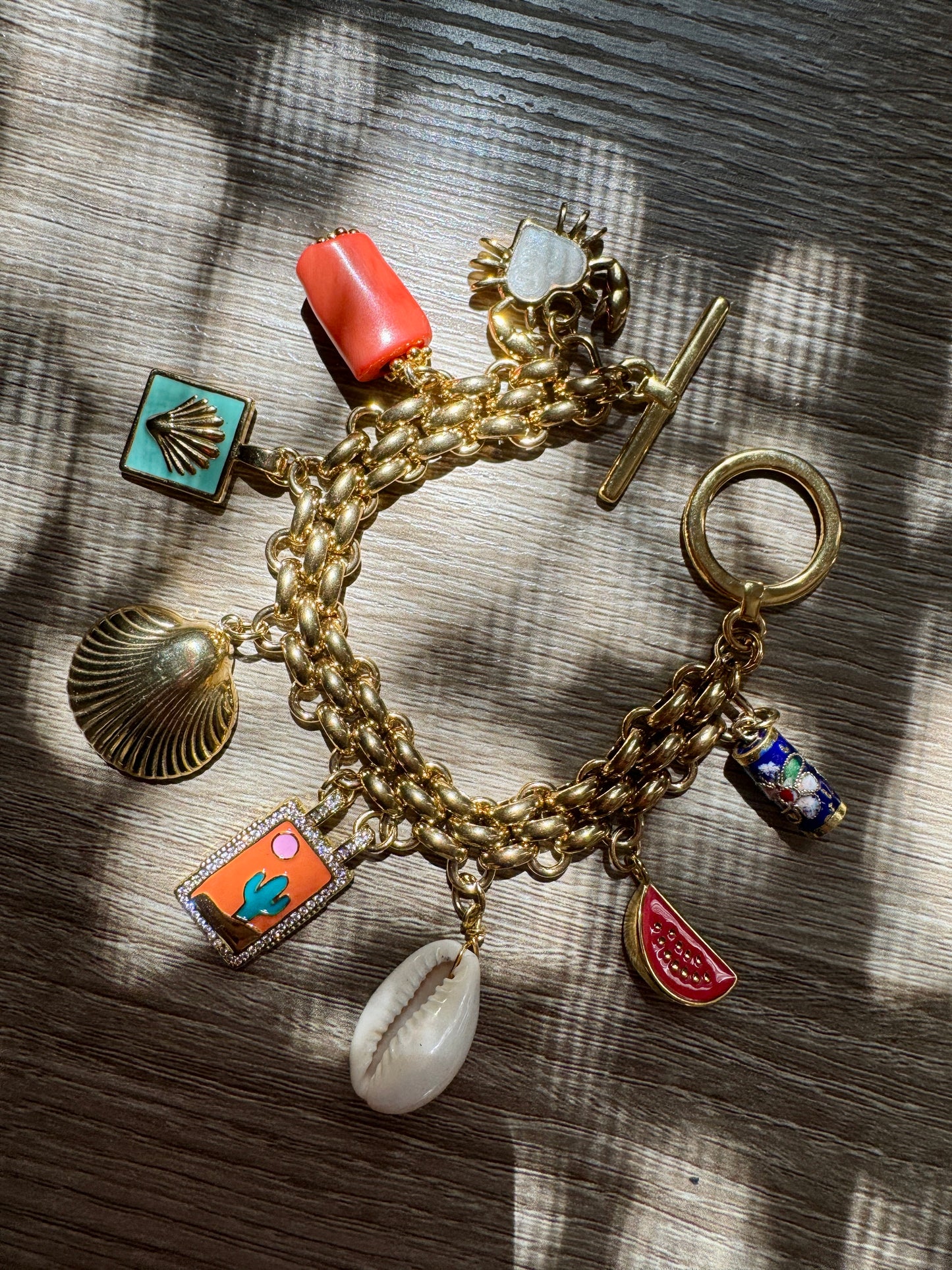 Gold charm bracelet with various summer charms on a wooden surface