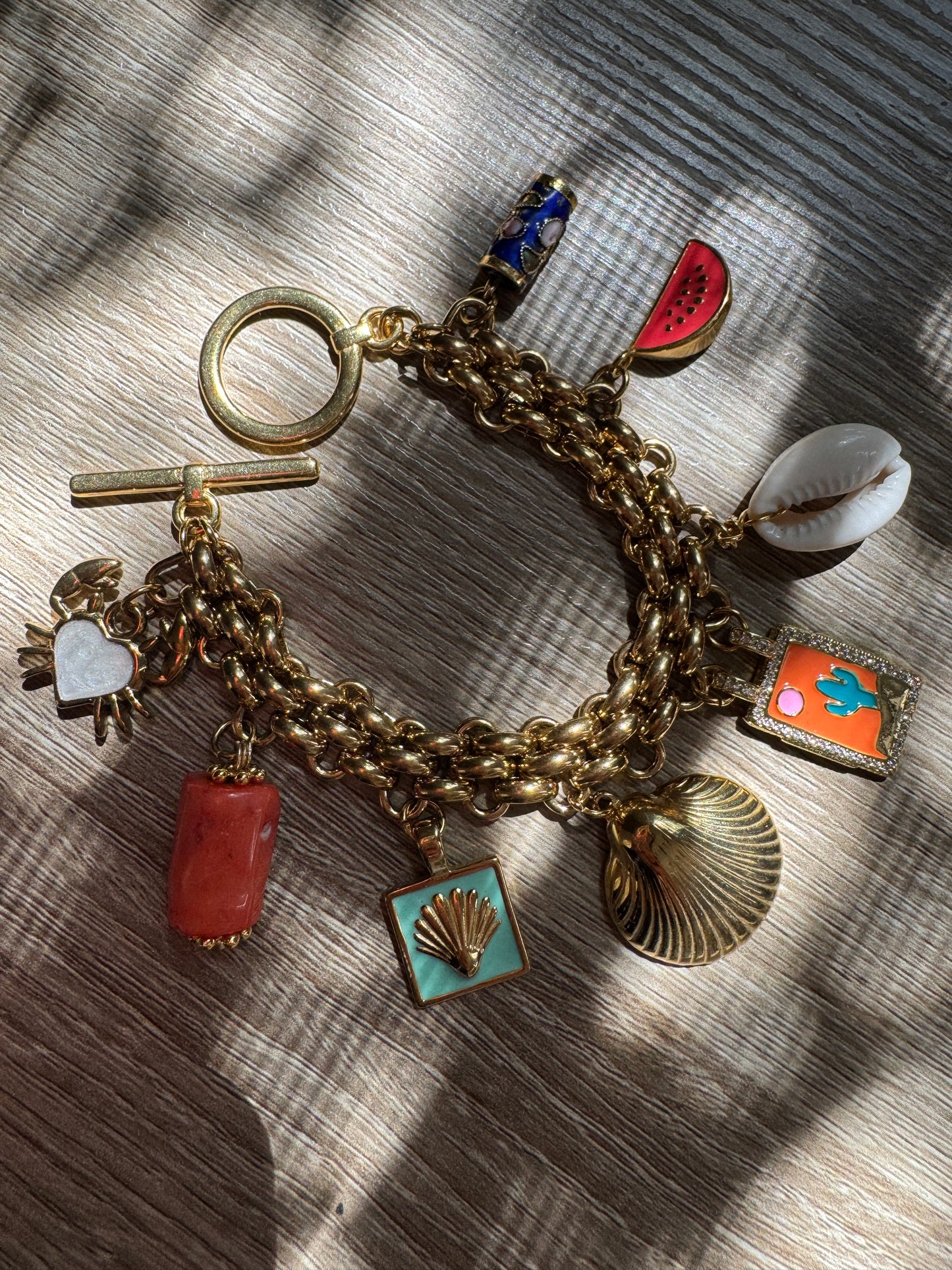 Gold charm bracelet with various summer charms on a wooden surface