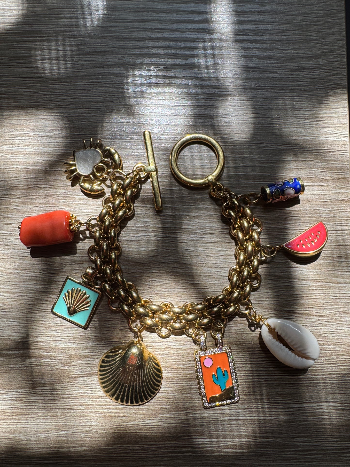 Gold charm bracelet with various summer charms on a wooden surface
