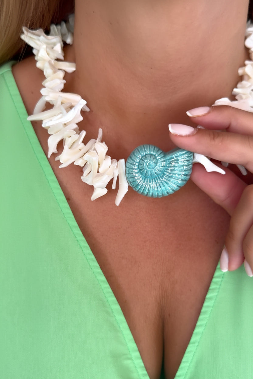 Close-up of a person wearing a green top with a white shell necklace and a blue seashell accessory.
