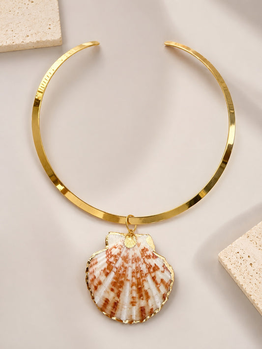Handmade gold-tone metal collar necklace with a dangling seashell pendant, displayed on a light beige surface with decorative stone tiles by LOTUS by M.  