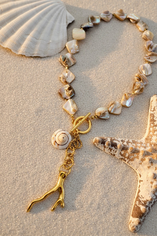 Shell necklace with a gold clasp on sand with a shell and starfish in the background