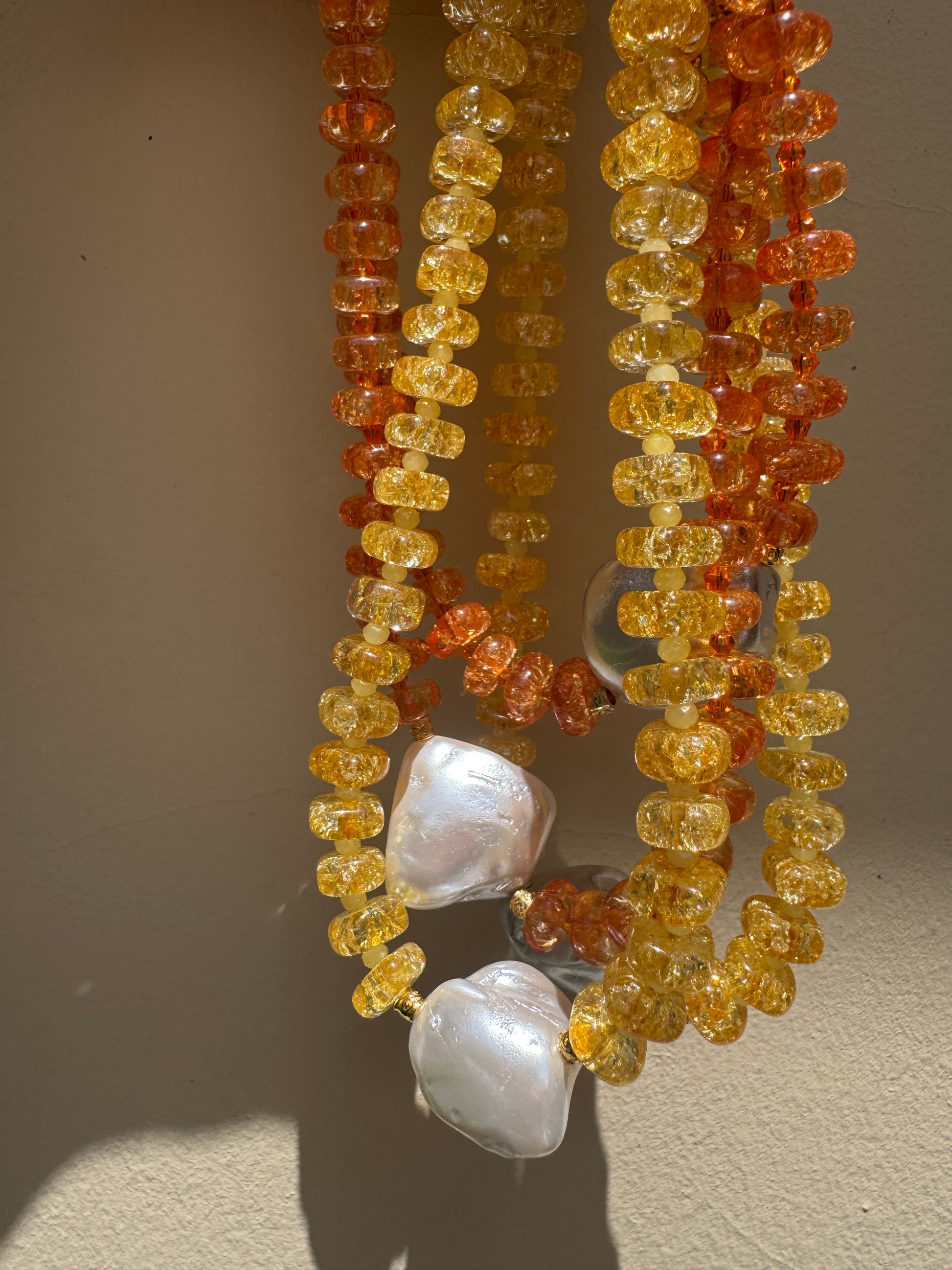 Necklace with orange and yellow crystal beads and a white mother of pearl on a beige background