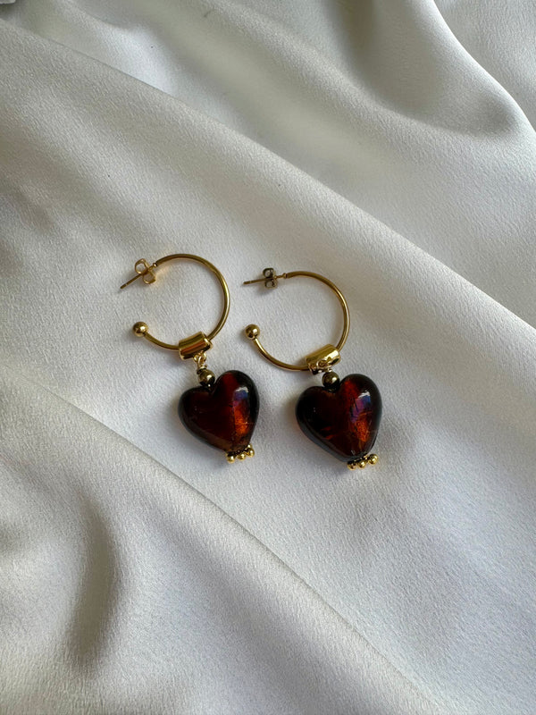 Gold hoop earrings with heart-shaped red stones on a white fabric background
