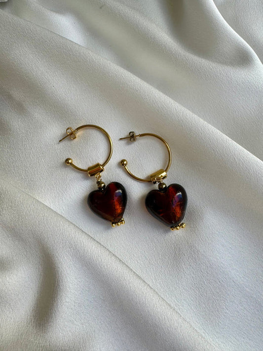 Gold hoop earrings with heart-shaped red stones on a white fabric background