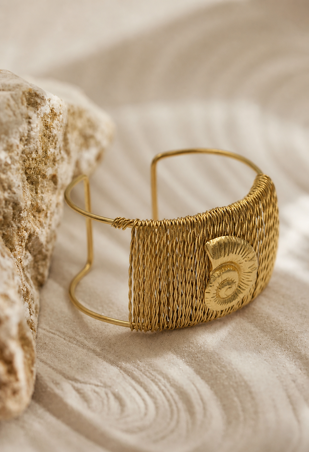 Gold bracelet with textured design on a sandy background