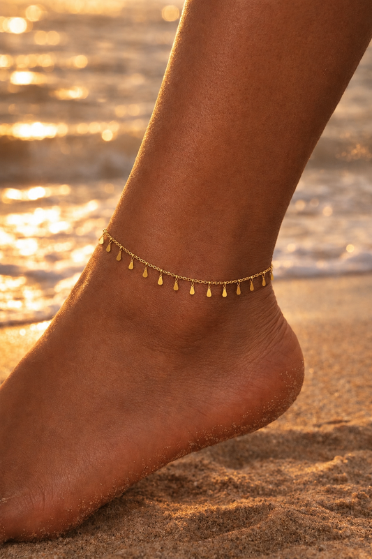 Gold anklet with vertical bars on a foot with a beach background