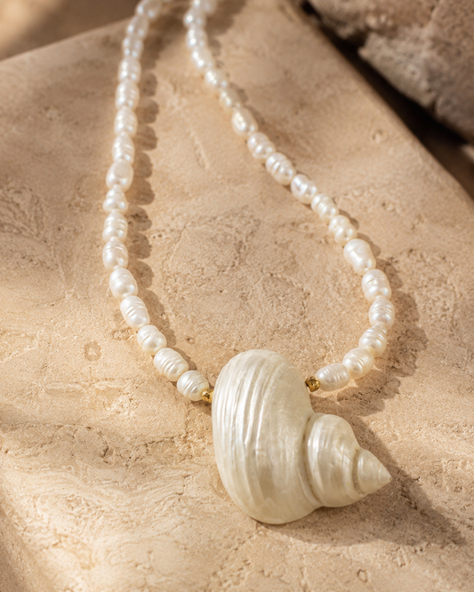 Pearl necklace with a shell pendant on a textured beige surface