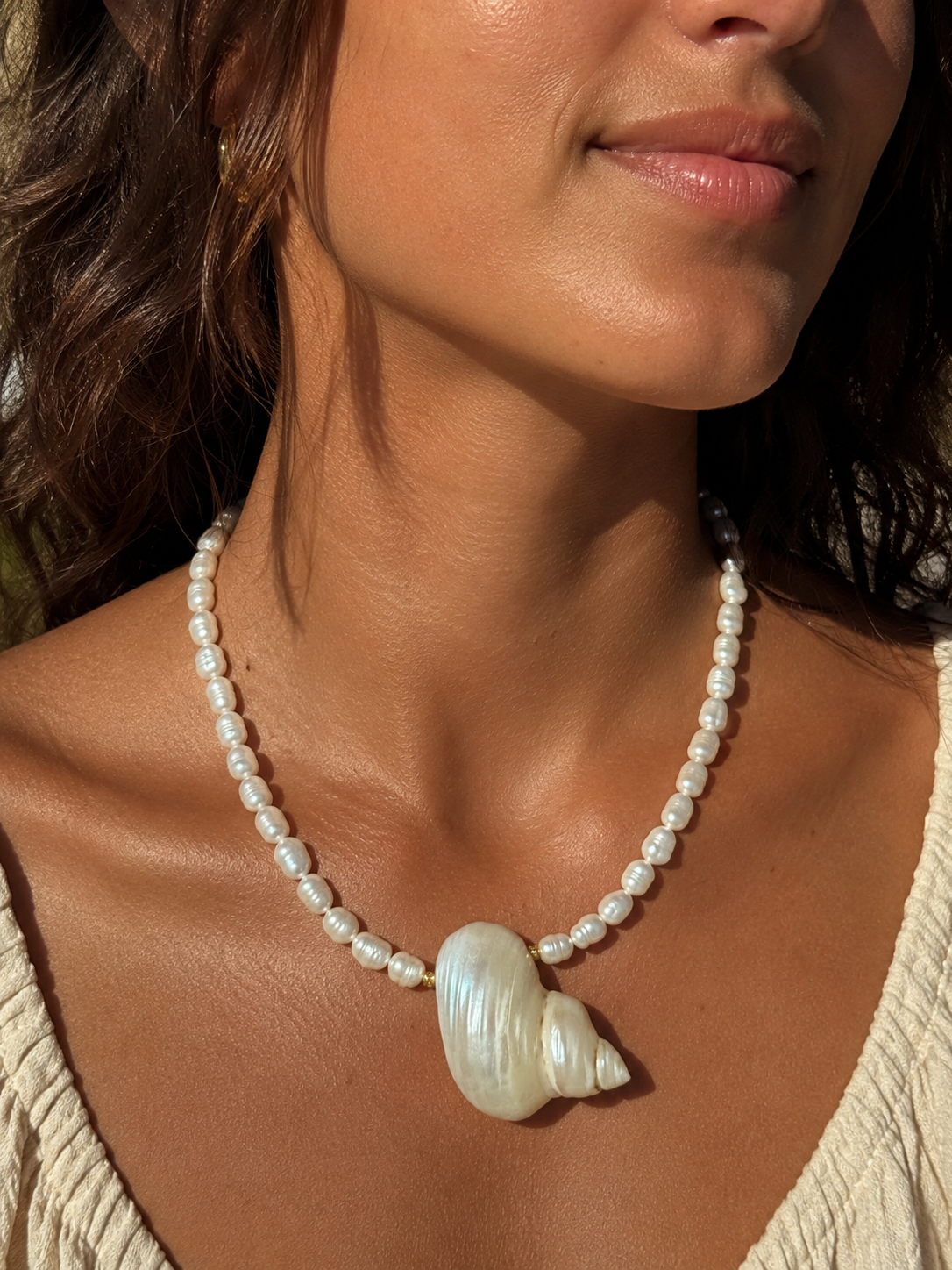 Close-up of a woman wearing a pearl necklace with a large shell pendant.