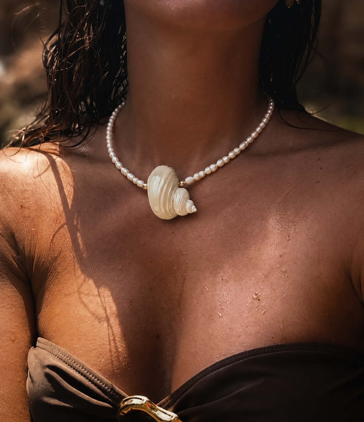 Pearl necklace with a large white natural shell in the middle worn by a person with bikini outdoors