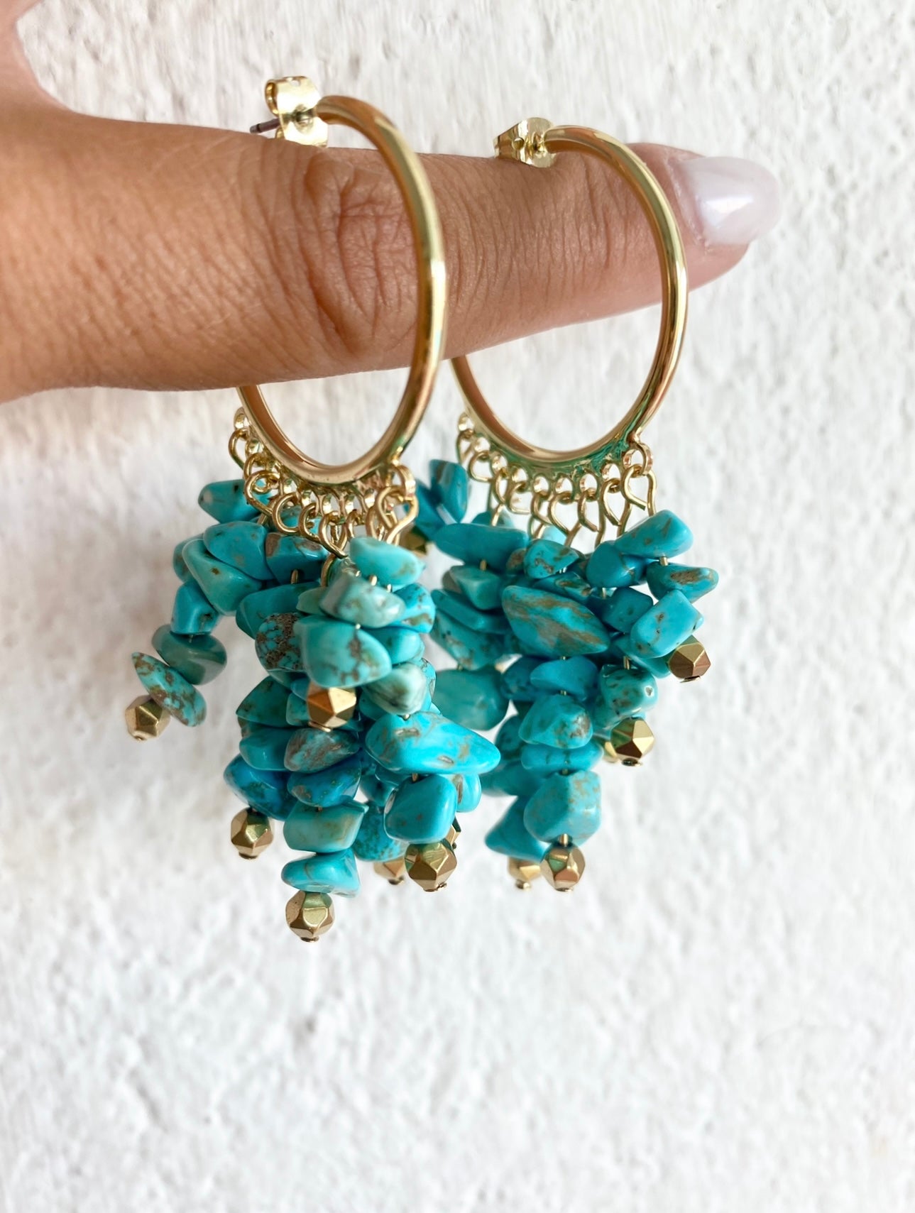 Handmade turquoise hoop earrings with gold-plated stainless steel by LOTUS by M hanging from a finger