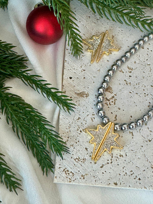 Necklace with star-shaped pendants on a textured surface with greenery and a red ornament.