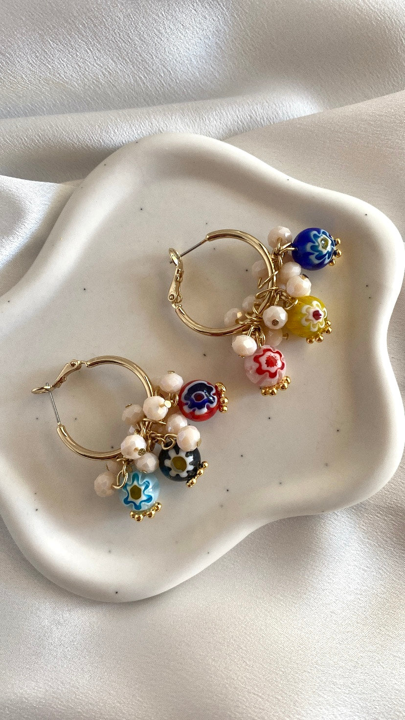 A pair of brass hoop earrings with millefiori glass beads and freshwater pearls, displayed on a white plate.