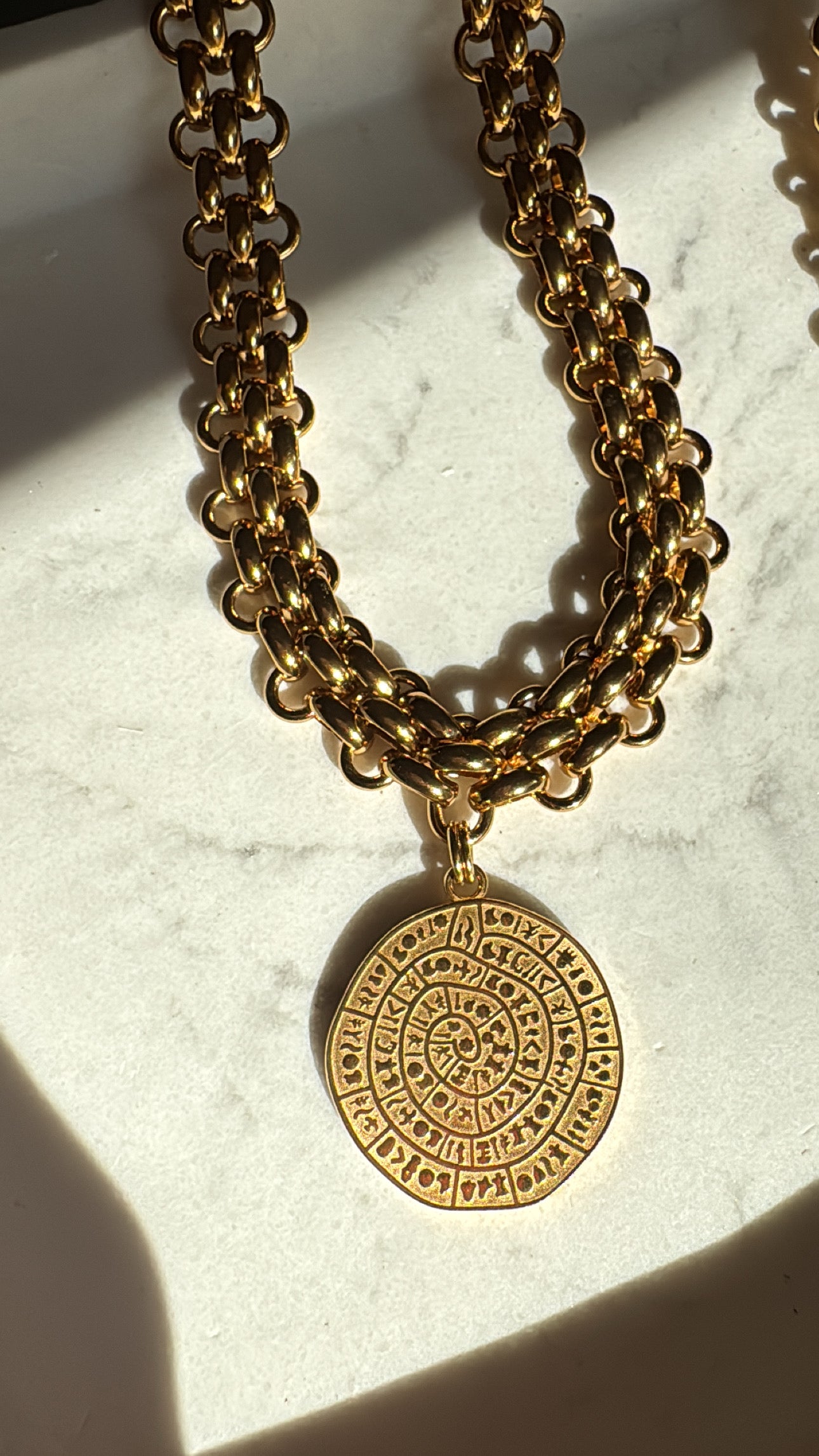 Gold chain necklace with a detailed pendant on a marble surface