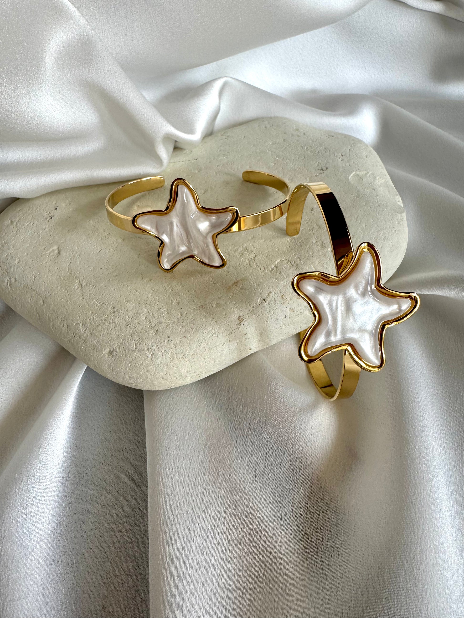 Two gold plated stainless steel bracelets with starfish designs in white enamel, displayed on a white surface.