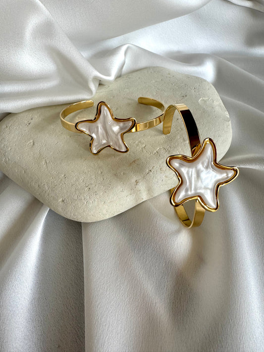Two gold plated stainless steel bracelets with starfish designs in white enamel, displayed on a white surface.