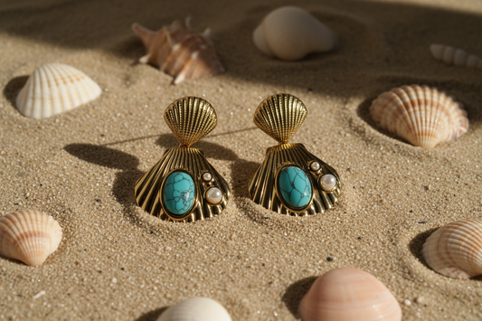 Gold shell earrings with turquoise stones on a sandy surface with seashells.
