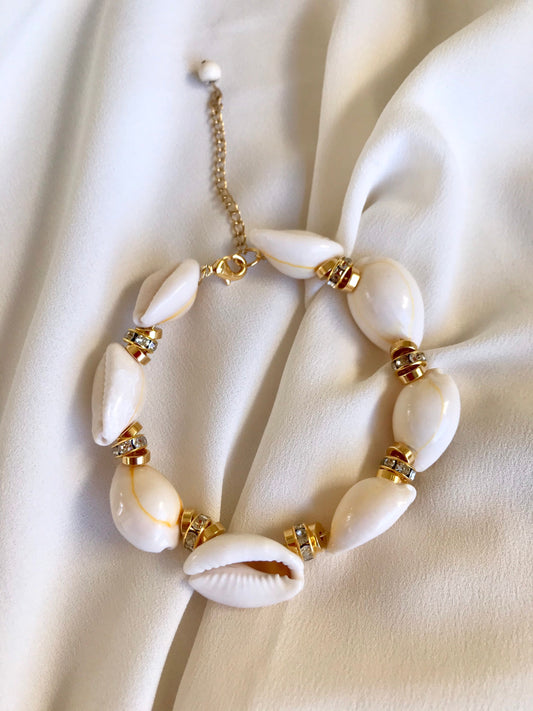 A St Tropez white shell bracelet with gold accents and crystals, displayed on a fabric surface.